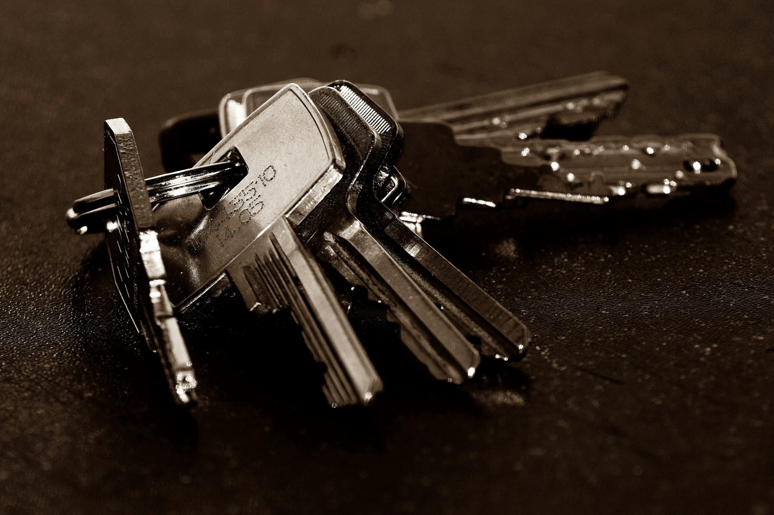 A detailed close-up of a bunch of metallic keys resting on a dark textured surface.